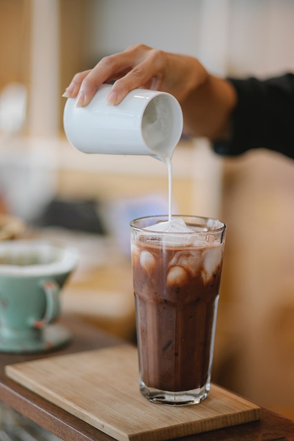 cold chocolate milk cup with ice and milk being poured in