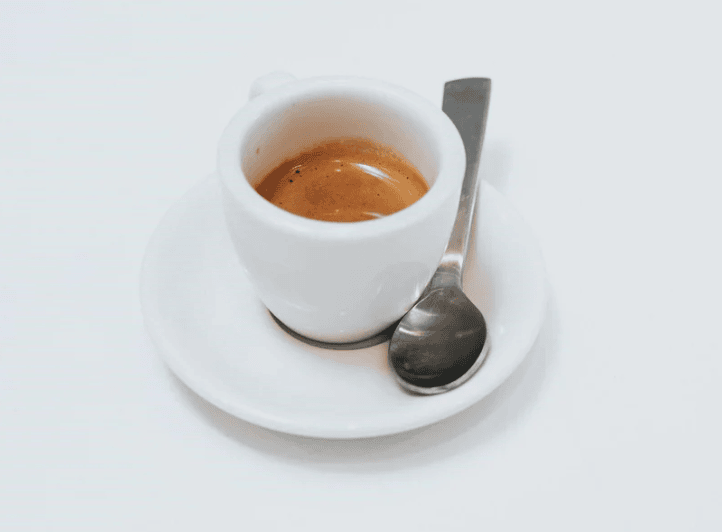 a single shot of espresso on a plate with a spoon
