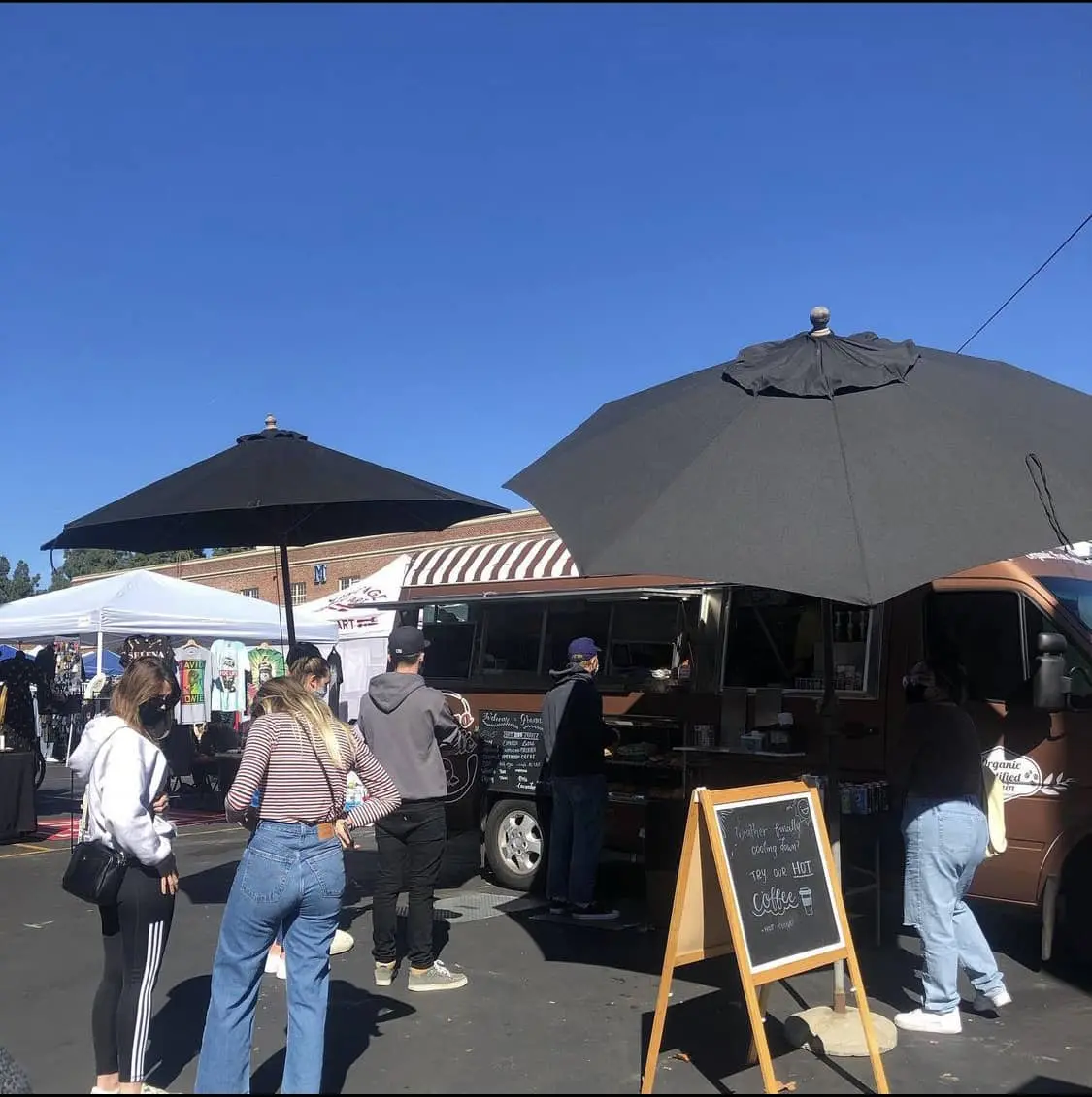Granno Cafe open with a line of patrons under two black shade umbrellas and a menu to the right.