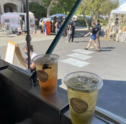 A shot from inside Granno Cafe of two iced beverages and market patrons walking by.